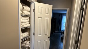 A hallway with a closet containing neatly folded towels and a white door. - Lake Retreat House (Anderson)