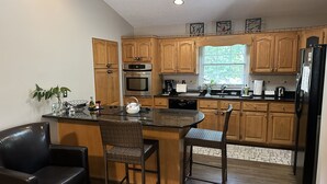 A kitchen with wooden cabinets, a black refrigerator, a built-in oven, and a window. - Lake Retreat House (Anderson)