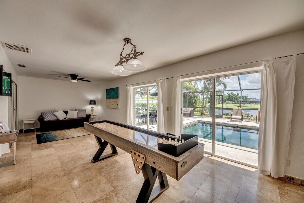 A spacious room with a foosball table, a ceiling fan, and a large window overlooking a swimming pool.