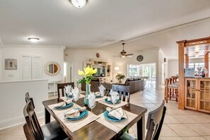 A dining area with a wooden table set for four, a vase with flowers, and a kitchen in the background.