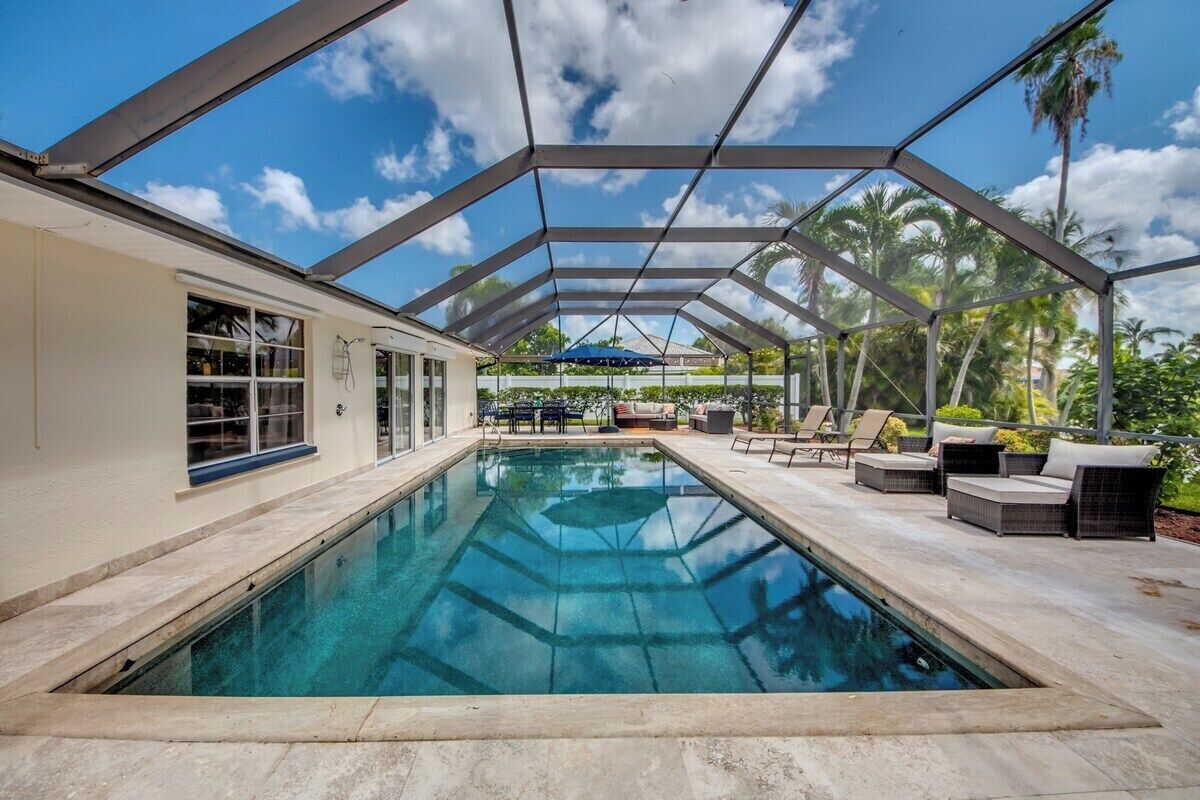 Ein überdachter Pool mit Glasdach, umgeben von Gartenmöbeln und Palmen.