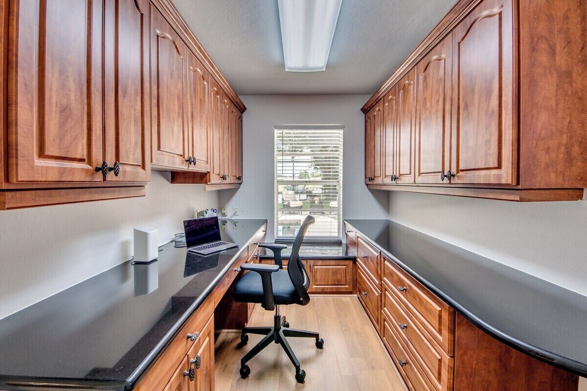 A narrow kitchen with wooden cabinets, a black countertop, and a window with blinds.