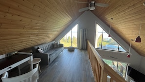 Une chambre confortable située sous les toits, avec un plafond en bois, une grande fenêtre, un ventilateur de plafond et un téléviseur.