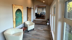 Un couloir doté d’un plancher en bois, d’une porte verte et d’un coin salon avec deux chaises.