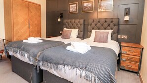Una cama doble con una colcha de cuadros grises y blancos, un armario de madera y una mesita de noche con cajones.