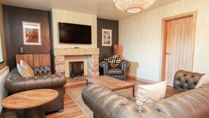 A living room with leather sofas, a wooden coffee table, a fireplace, and a flat-screen TV mounted above it. - Eldroth (Skipton)