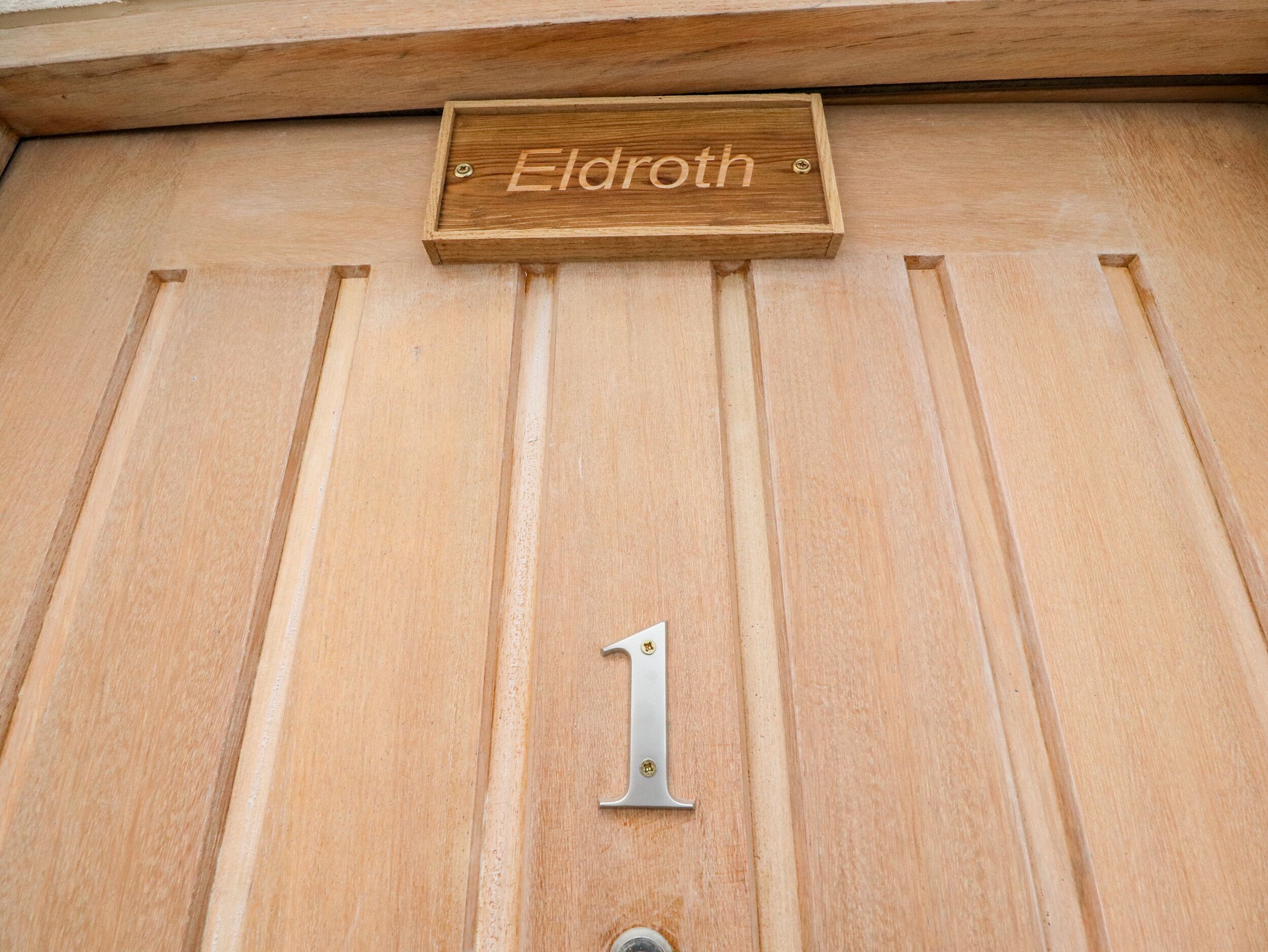 A wooden door with a nameplate reading "Eldroth" and a metal number plate with the number "1".