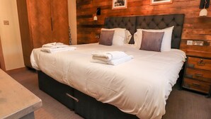 A neatly made bed with white linens and towels, a dark upholstered headboard, wooden paneling on the wall, and a wooden wardrobe. - Eldroth (Skipton)