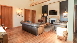 Amplia sala de estar con suelo de madera, sofás de cuero, chimenea y televisor montado en la pared.