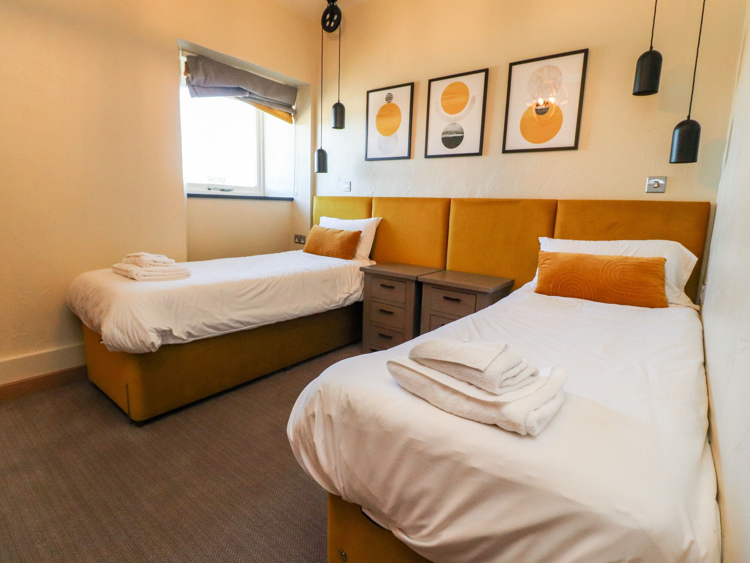 Une chambre d’hôtel avec deux lits simples, une table de chevet, une fenêtre donnant sur un paysage agréable et trois œuvres d’art encadrées accrochées au mur.