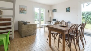 A dining area with a wooden table and chairs, a wicker sofa, and a green plastic chair. - LES AJONCS - 300m de la plage - Parking (Batz-sur-Mer)