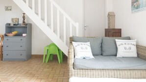 A living room with a wicker sofa, a grey cabinet, a green chair, and a staircase. - LES AJONCS - 300m de la plage - Parking (Batz-sur-Mer)