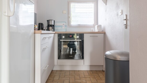 A compact kitchen with white cabinets, a Bosch oven, a coffee maker, and a window with blinds. - LES AJONCS - 300m de la plage - Parking (Batz-sur-Mer)