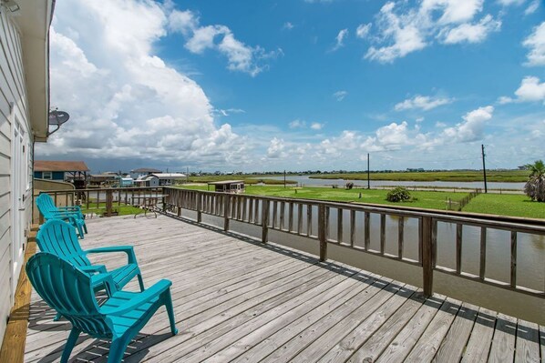 A wooden deck with turquoise Adirondack chairs, a railing, and a view of a river and distant buildings.