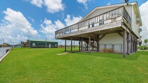 A two-story building with a balcony, a grassy lawn, and a body of water in the background. - Fabulous Views, Updated, Minutes to ICW & Beach (Bay City)