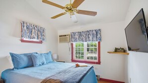 Un dormitorio con cama, ventilador de techo, ventana con contraventanas y televisor montado.