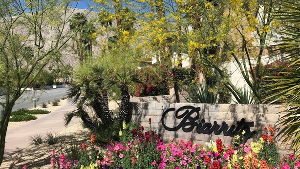 Un letrero con el nombre 'Biartis' rodeado de diversas plantas con flores y palmeras.