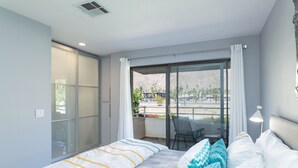 Un dormitorio moderno con una cama grande, una puerta corrediza de vidrio a un balcón y vistas al exterior.