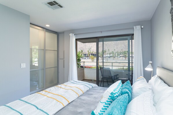 A modern bedroom with a large bed, a sliding glass door to a balcony, and a view of the outdoors. - Biarritz Escape (Palm Springs)