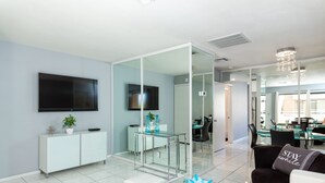 Un salón moderno con una mesa de centro de vidrio, sofá blanco y un televisor montado en la pared.