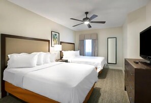 Two single beds with white linens and wooden headboards, a flat-screen TV, and a ceiling fan.