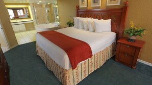 Een hotelkamer met een groot bed, een houten nachtkastje, een spiegel, een badkamer met douchecabine van glas en een kleine potplant.