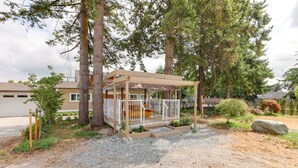 A covered outdoor area with a wooden deck, surrounded by trees and a gravel path. - Superb Convenient North Delta Vacation Home with 6 Bed and 6 Bath (Delta)
