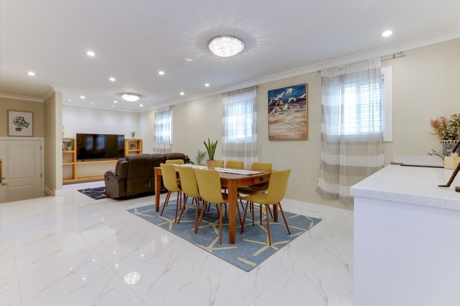 A modern living room with a dining area, a sofa, a flat-screen TV, and a painting on the wall.