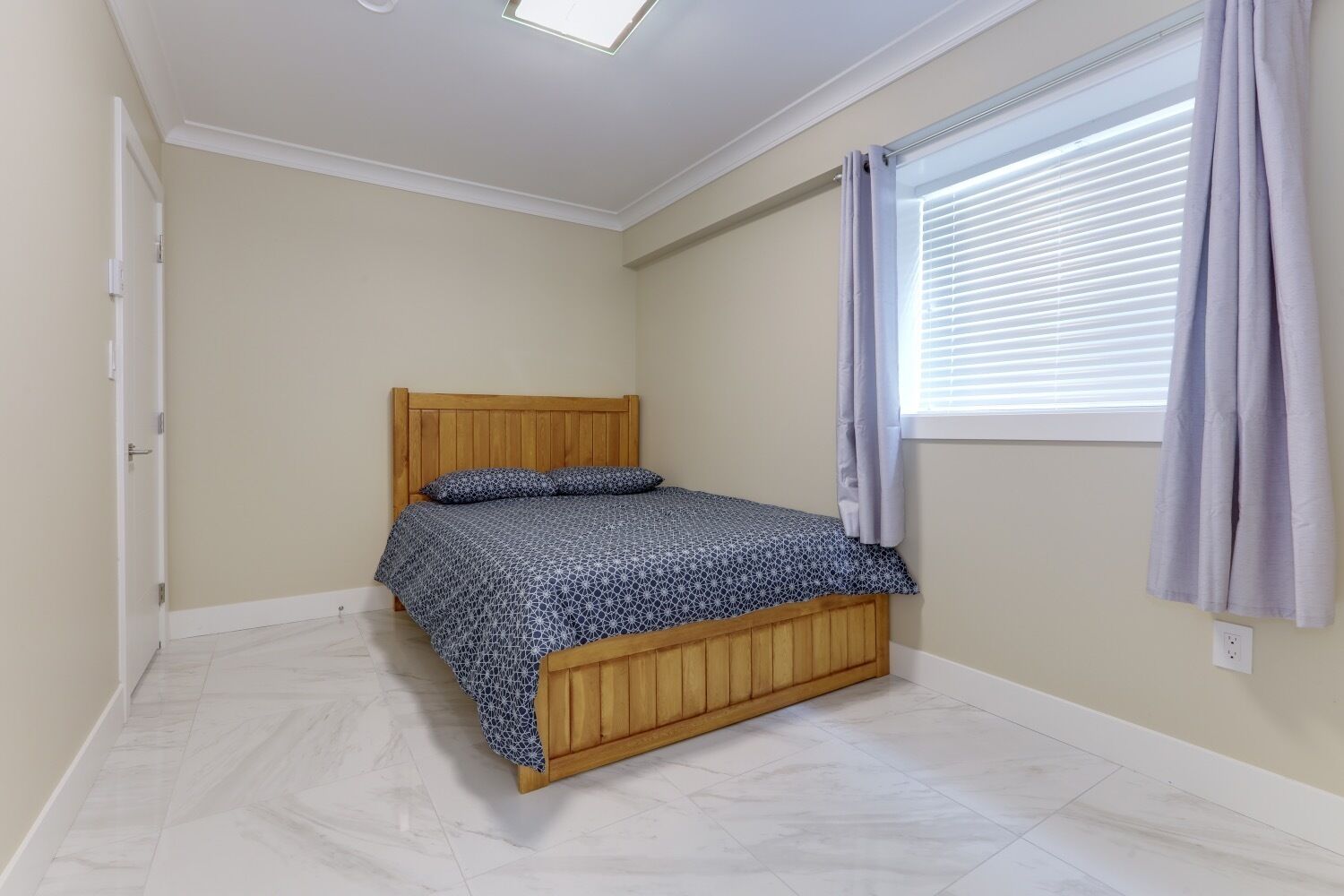 Quarto com cama de madeira, janela com persianas e porta.