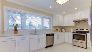 A modern kitchen with white cabinets, stainless steel appliances, and a window with blinds. - Superb Convenient North Delta Vacation Home with 6 Bed and 6 Bath (Delta)