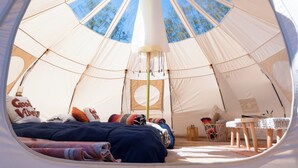 Interior acogedor de una tienda en forma de cúpula, con cama, almohadas, una mesita y una lámpara colgante.