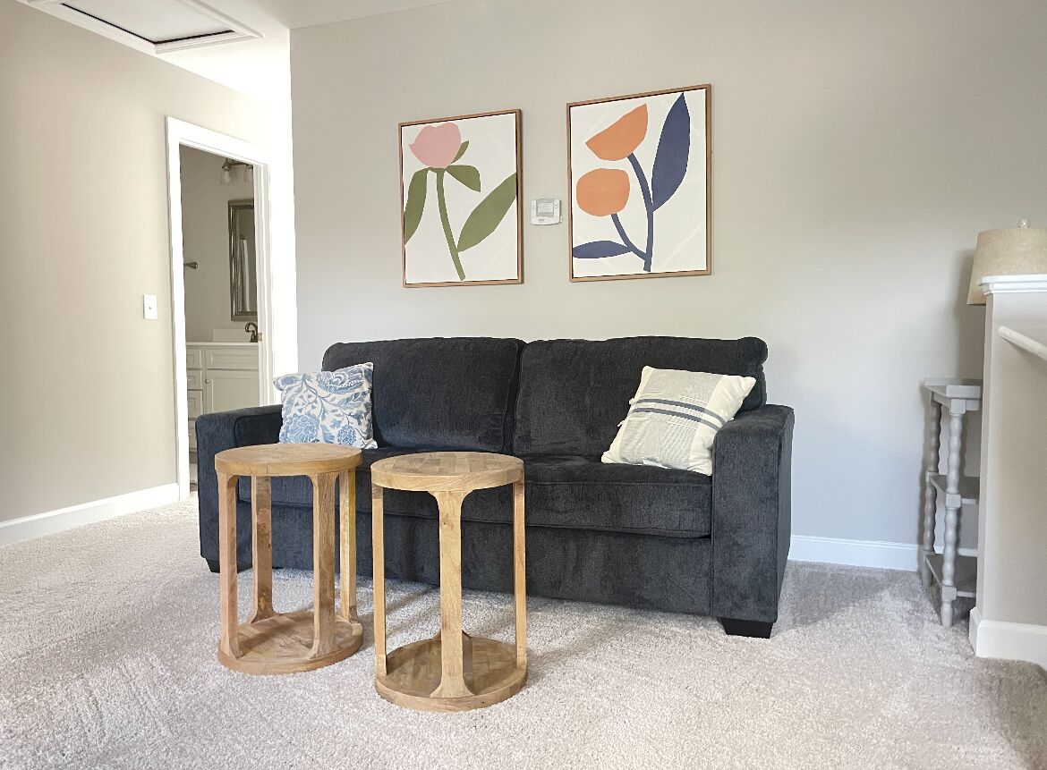 A living room with a dark grey sofa, two wooden side tables, and two framed floral artworks on the wall.