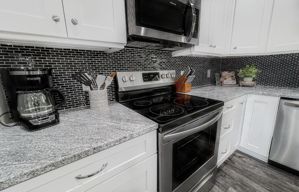A modern kitchen with white cabinets, a black microwave, a stainless steel stove, and a coffee maker.