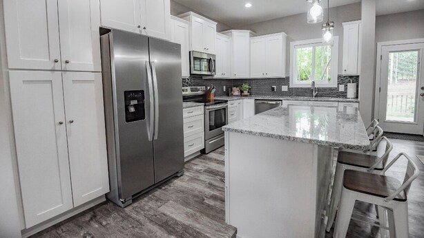 A modern kitchen with white cabinets, stainless steel appliances, a granite countertop, and a large island with bar stools. - NEW! Pinehurst Eight Sleeps 10! (Pine Hurst)