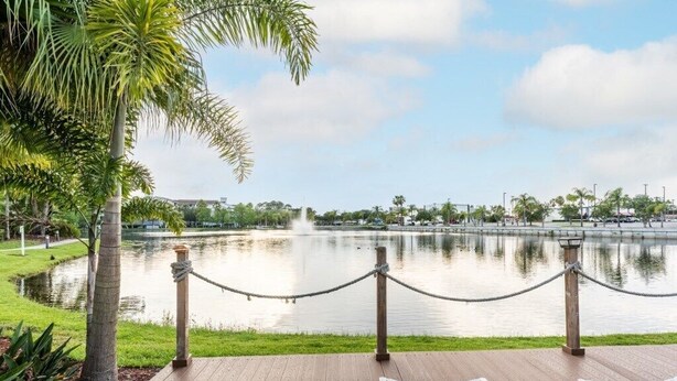 A waterfront deck with lounge chairs, a rope barrier, and a calm lake with a fountain.