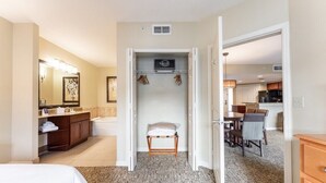 A hotel room with a bed, a bathroom with a sink and mirror, a closet with a hanging rack, and a view into the kitchen area.