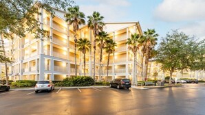 A multi-story hotel with balconies, palm trees, and a parking lot.