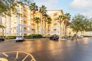 A multi-story hotel with balconies, palm trees, and a parking lot.