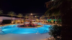 A nighttime view of a hotel pool area with a circular pool, palm trees, and a building with illuminated windows. - Las Vegas | Pool & Strip Access | Contemporary City Stay (Las Vegas)