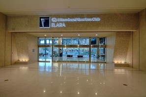 Un vestíbulo amplio con entrada de vidrio, un letrero de Hilton Grand Vacations Club ELARA y una vista despejada al exterior.