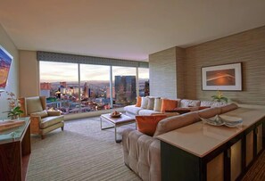 Enjoy a panoramic city view from the comfort of this spacious room, featuring a seating area with sofa and armchairs, coffee table, and dining table.