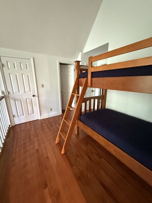 A room with a bunk bed, wooden flooring, a white door, and a staircase leading to another room.