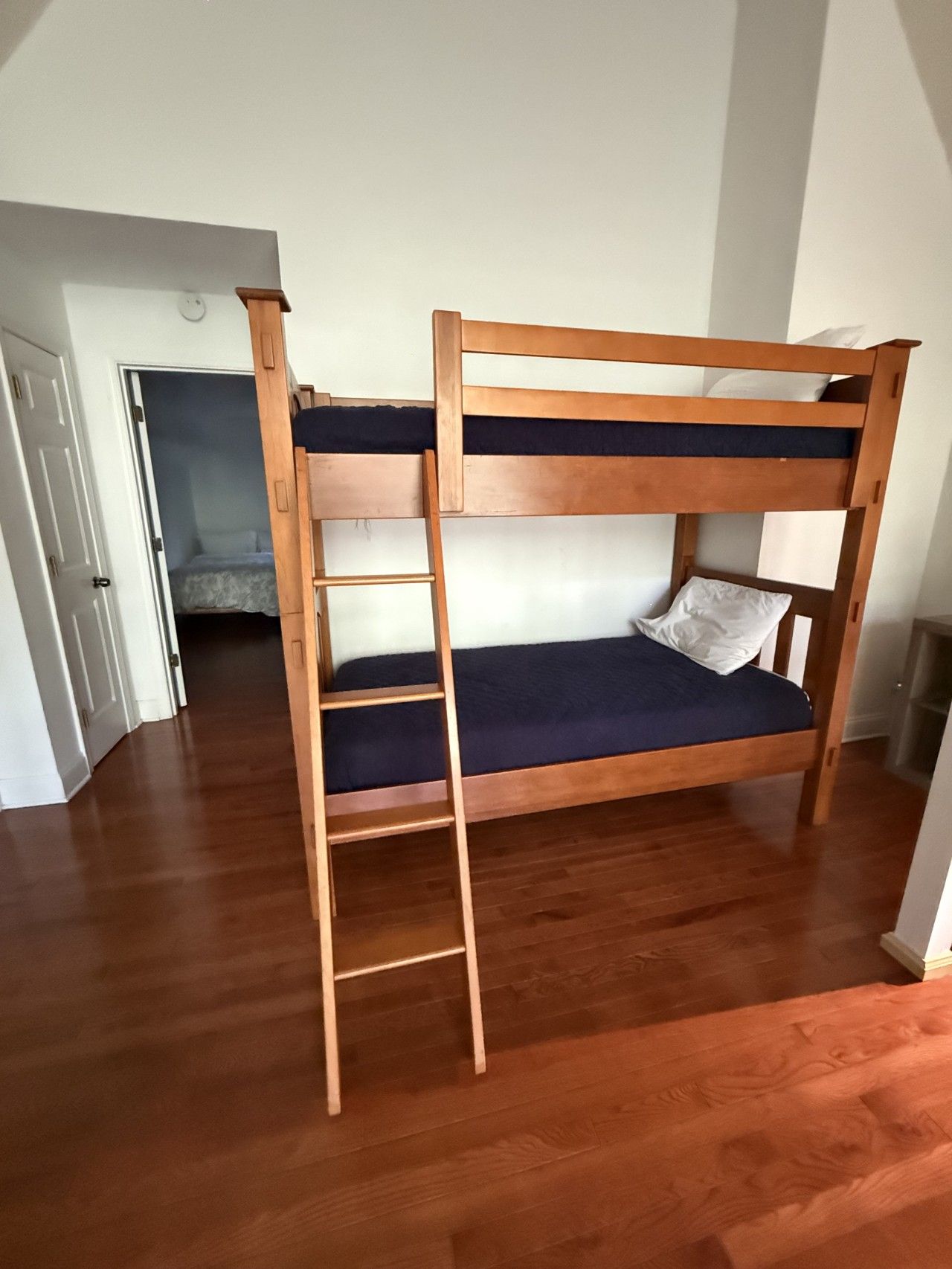 Een stapelbed met een ladder, houten vloeren en een deur naar een andere kamer.