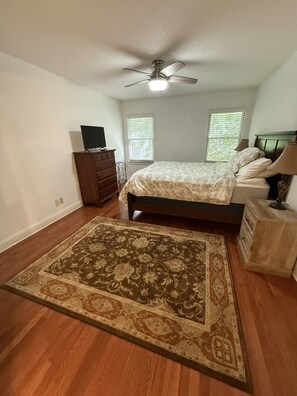 Quarto com cama, ventilador de teto, cômoda, televisão e janela com persianas.