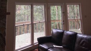 Ein Zimmer mit einem großen, raumhohen Fenster mit Blick auf eine Terrasse und einen Wald.