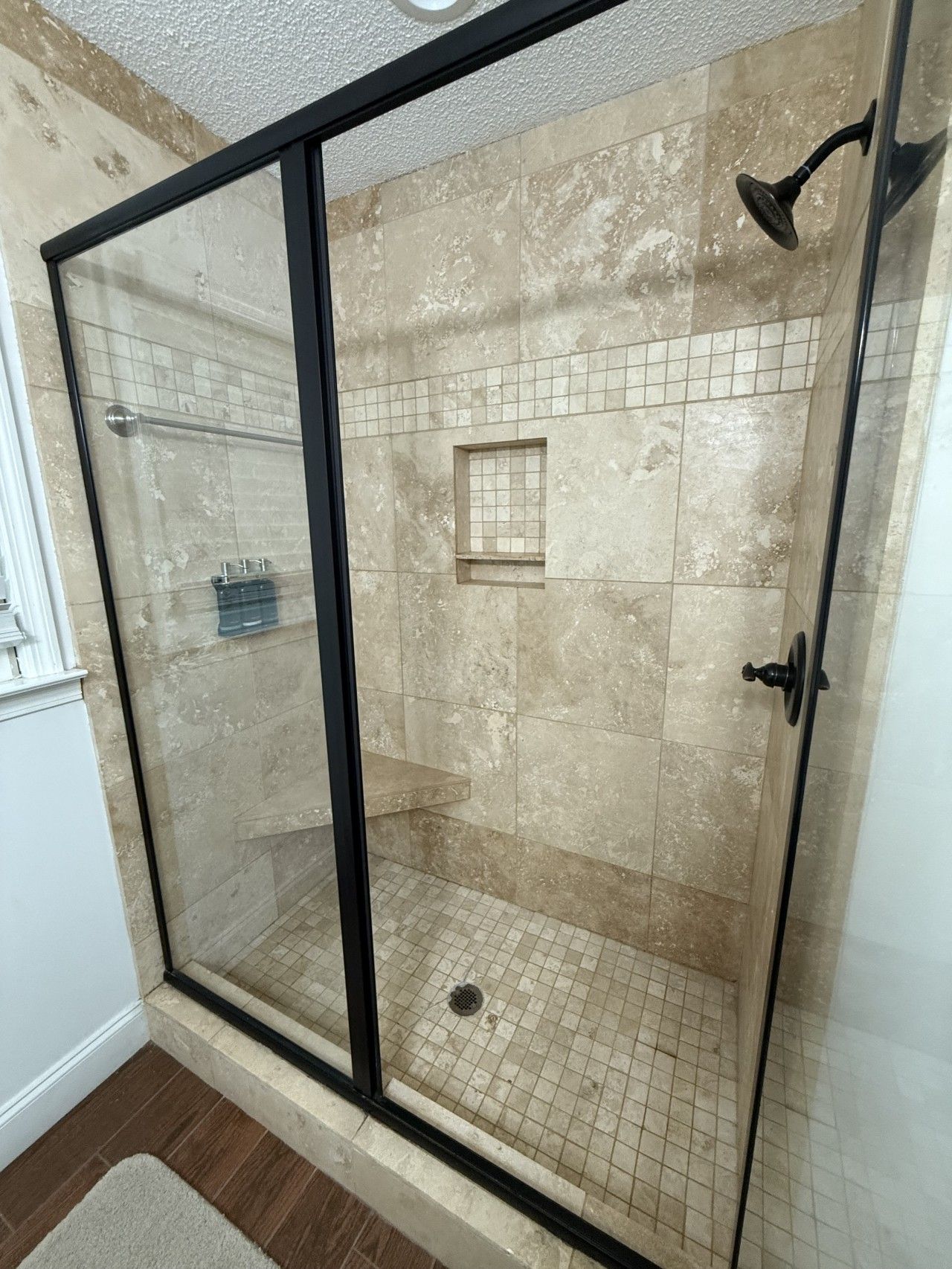 Une douche fermée par des parois en verre, avec un sol carrelé et une petite fenêtre.
