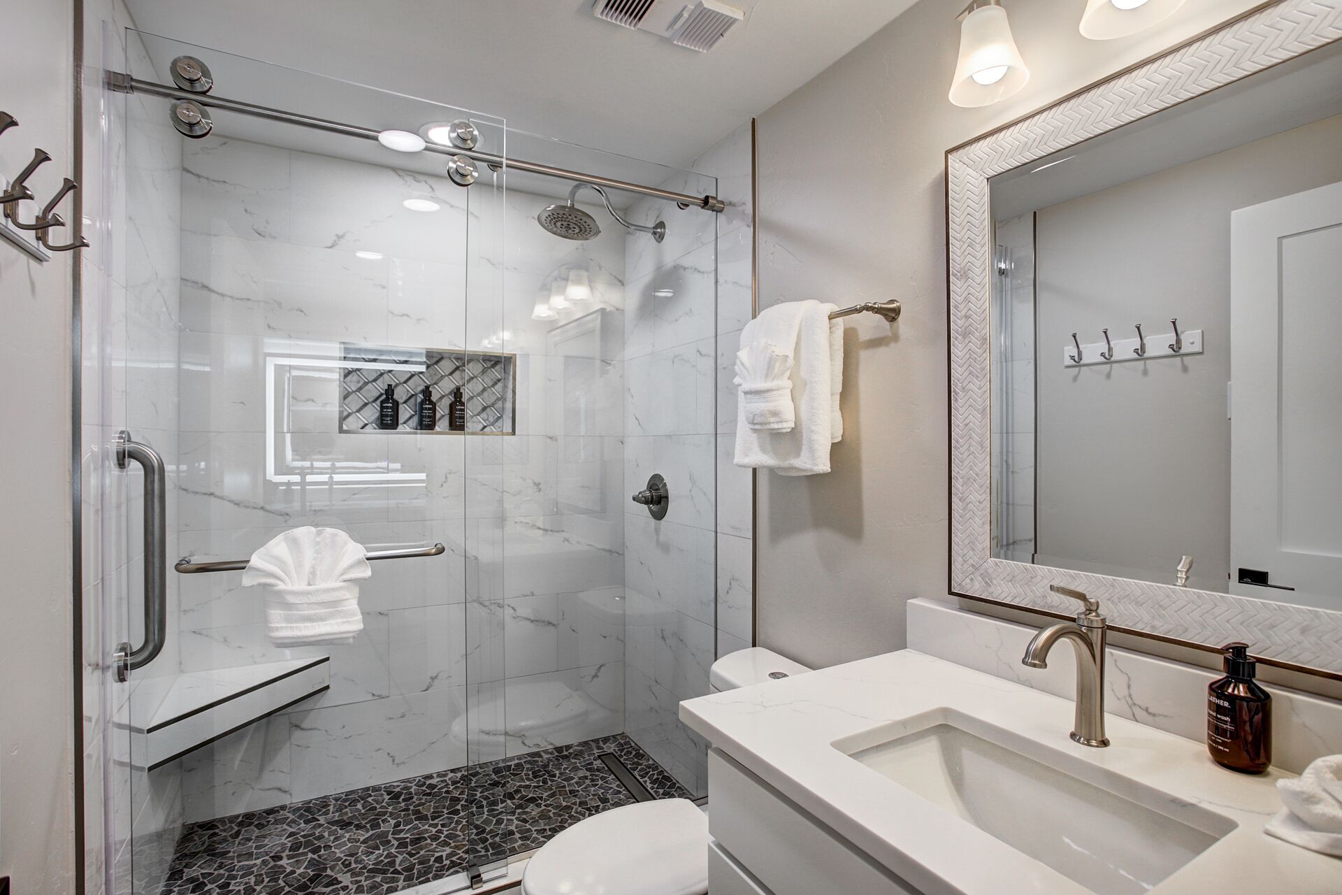 Uma casa de banho moderna com cabine de chuveiro em vidro, lavatório branco e espelho grande.