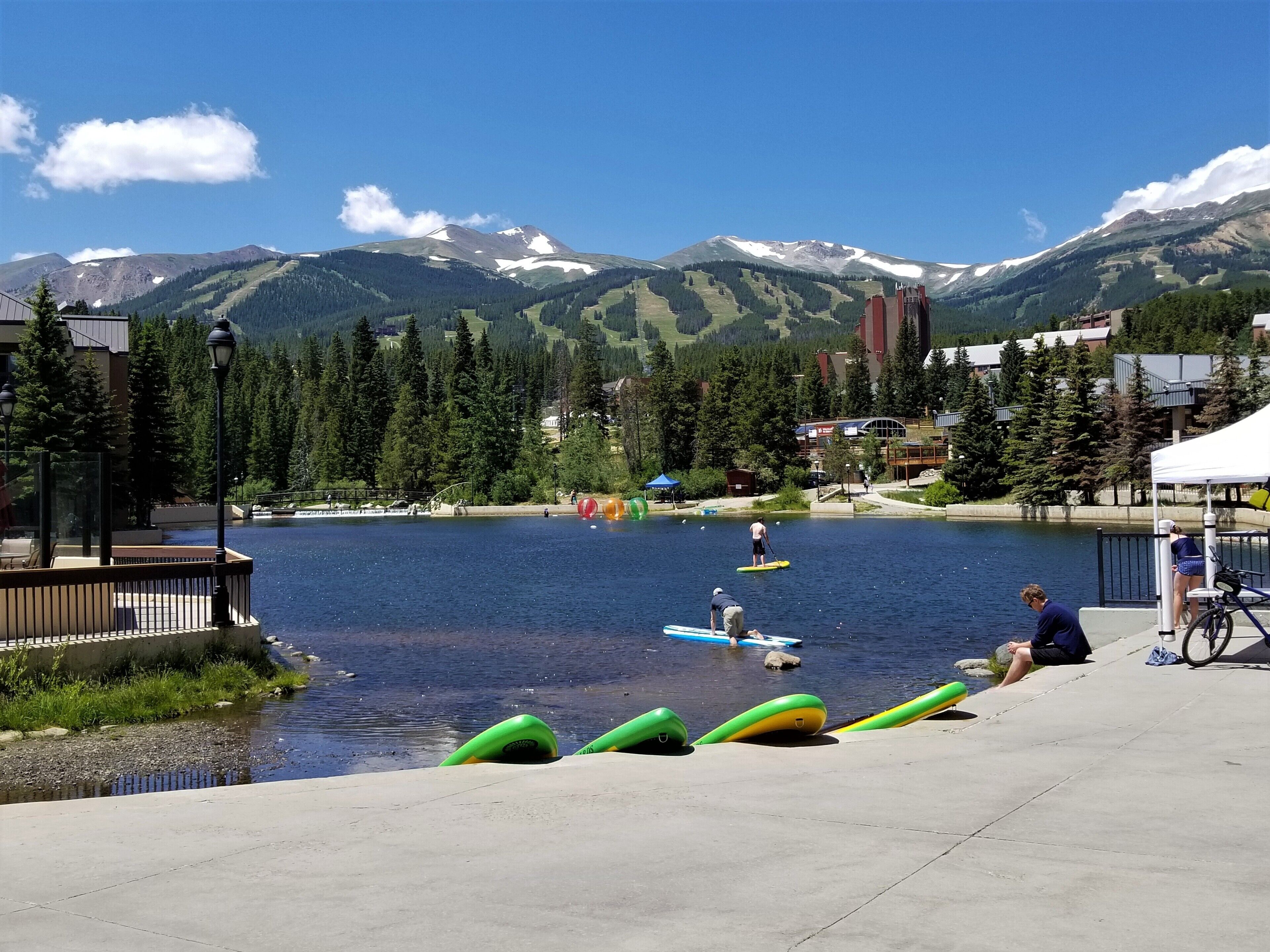 A lakeside view with a dock, kayaks, and a mountainous backdrop.