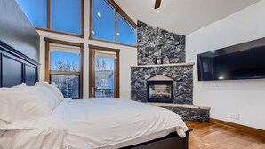 Een slaapkamer met een groot bed, een stenen openhaard en een aan de muur bevestigde televisie.