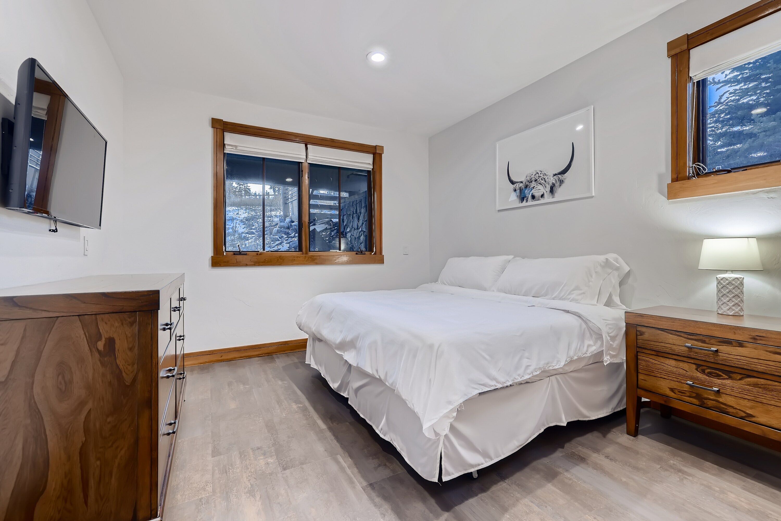Una camera da letto con un letto, una cassettiera in legno, una TV montata a parete e una finestra vista alberi.